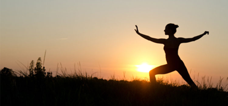 woman silhouetted performing yoga pose at sunset