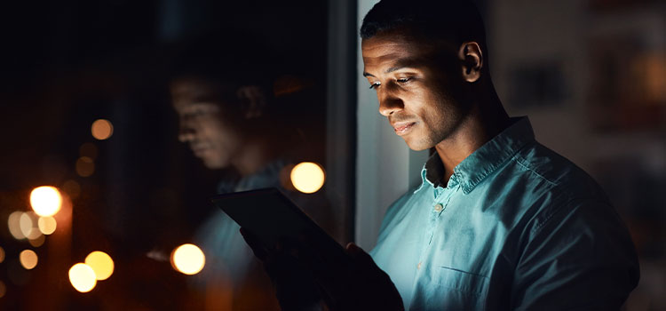 person standing at window at night looking at tablet