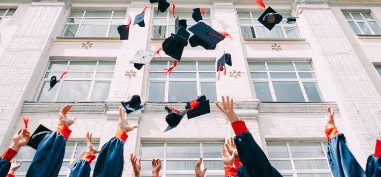 students throwing graduation hats in the air outside university