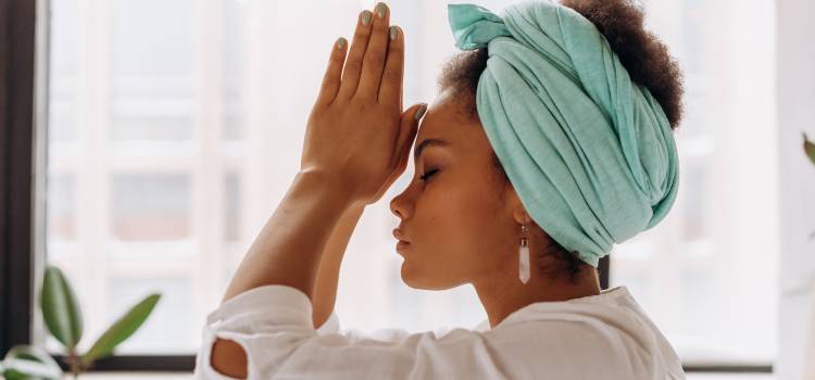 woman with eyes closed and teal towel on head with hands in praying position to her forehead