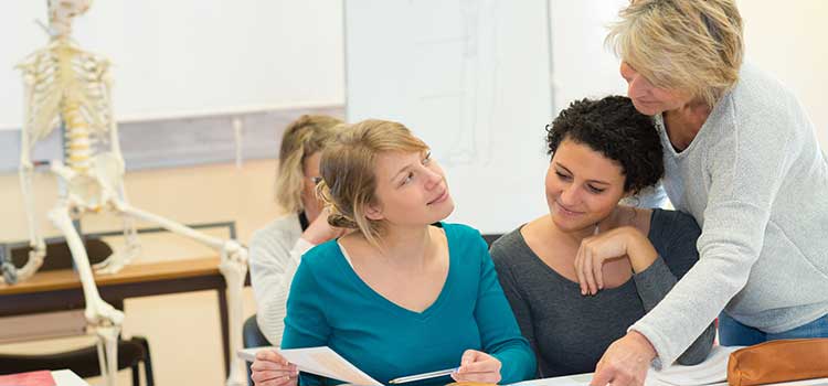 women in chiropractic class conferring with teacher