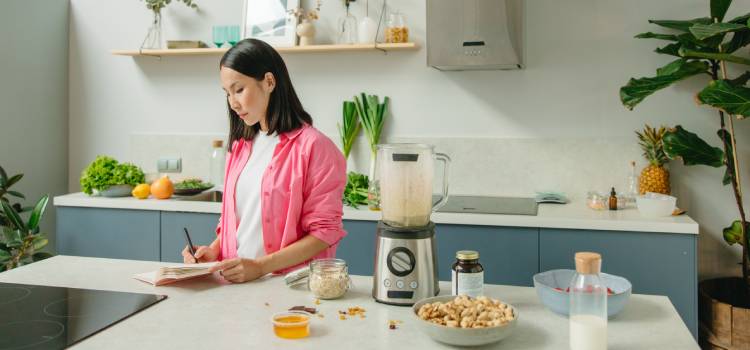 a nutritionist writing in her notebook at a counter with a blender