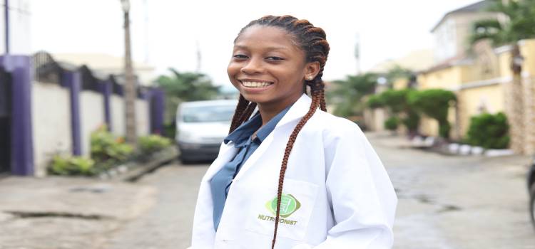 smiling female with braided hair and a lab coat that says nutritionist on it