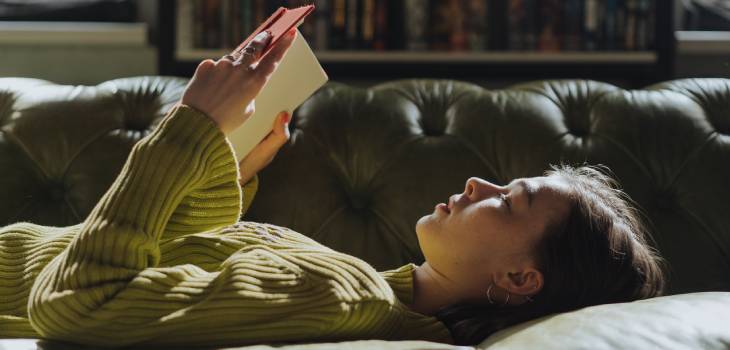 woman laying down on a leather sofa and reading a book to increase her knowledge