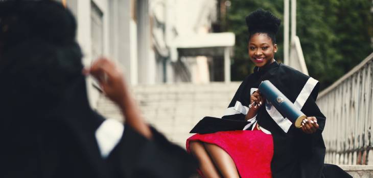 woman smiling in front of a university stairs holding her certificate in a tube