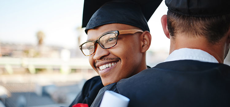 smiling young man hugs friend after earning bachelors degree