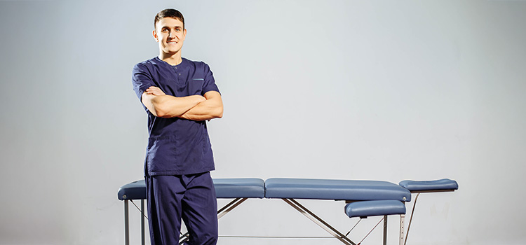 male massage therapist stands in front of his massage table with arms folded