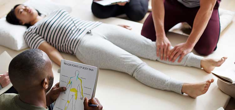 two massage therapy students practice massage using an anatomical chart on a fellow classmate