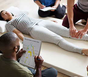 two massage therapy students practice massage using an anatomical chart on a fellow classmate
